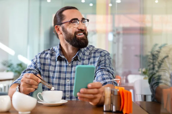 Bebaarde man zetten wat suiker in zijn koffie zittend in cafetaria — Stockfoto