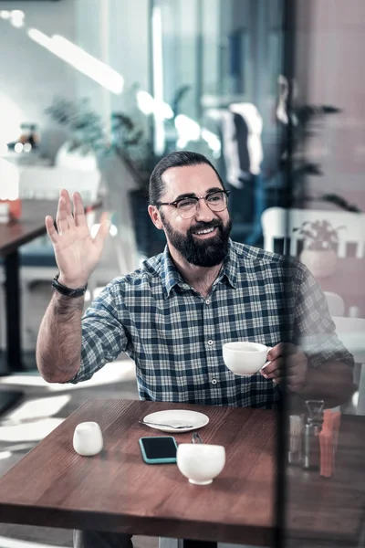 Baard stralende man verhogen van zijn hand vergadering collega in cafetaria — Stockfoto