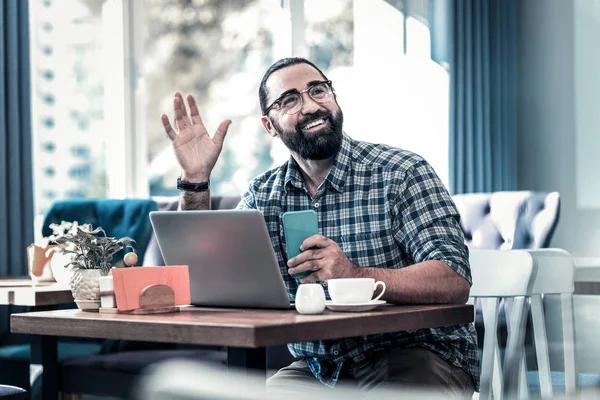 Beaming freelance writer smiling and waving his friend meeting friend