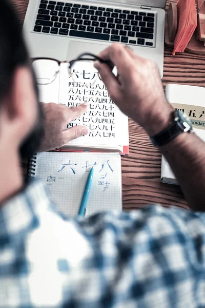 Вид сверху на человека в квадратной рубашке и наручных часах, изучающих иероглифы — стоковое фото