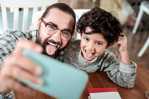 Dark-eyed father and son showing their tongues making selfie together — Stock Photo, Image