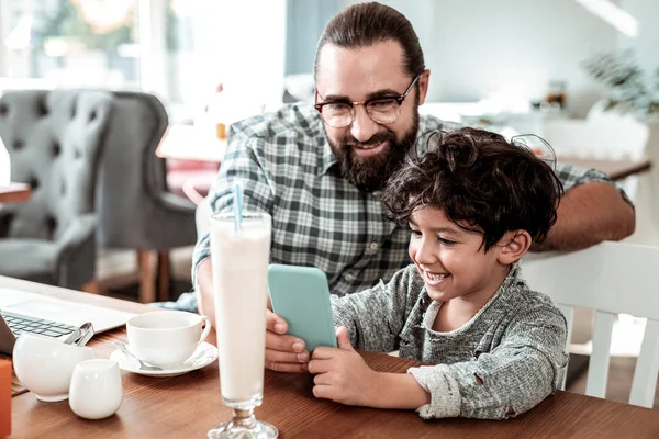 Χαριτωμένο ακτινοβολούν γιος του κρατώντας τα μπλε smartphone ενώ παίζετε online παιχνίδι — Φωτογραφία Αρχείου