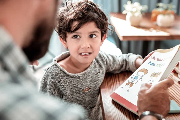 Funny cute boy feeling concerned while studying reading with father