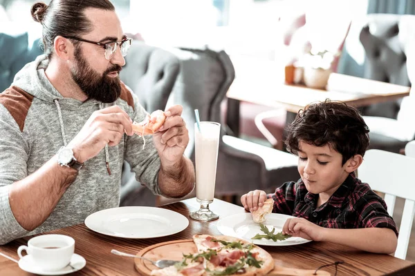 Бородатий батько і милий смішний син весело їсть піцу разом — стокове фото
