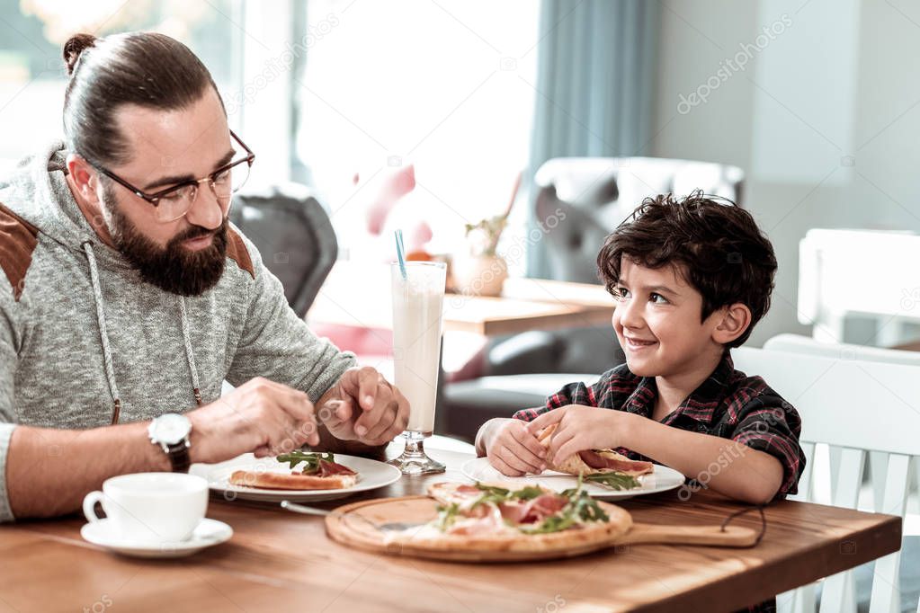 Father and son eating extremely yummy pizza with bacon and cheese
