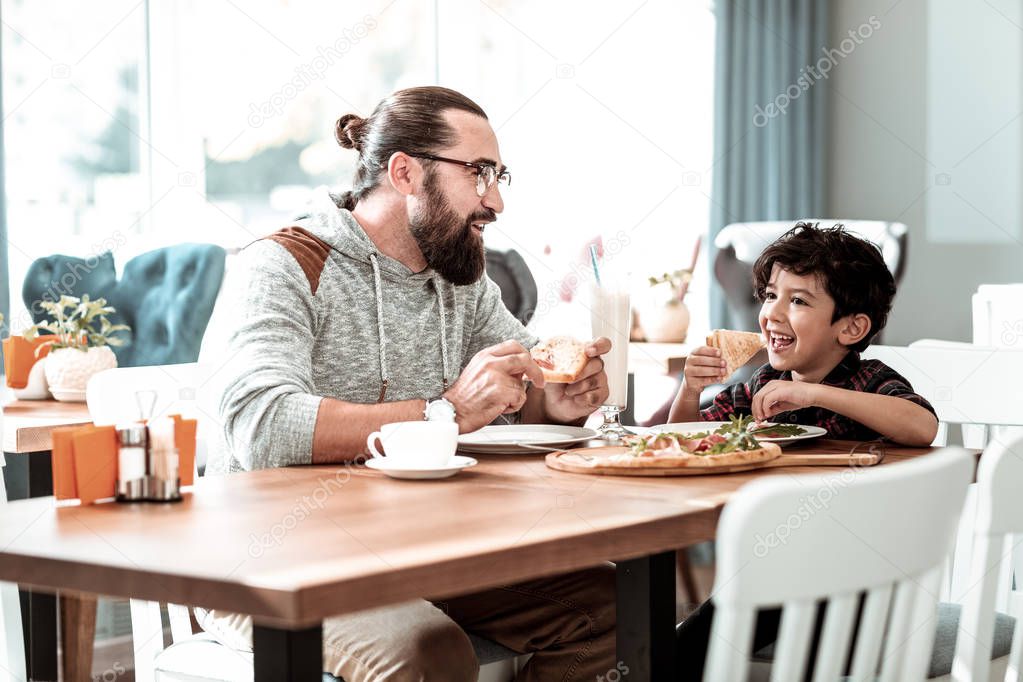 Good-looking handsome little boy eating cheesy yummy pizza