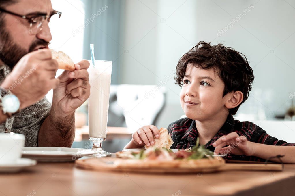 Bearded father giving extra piece of bacon his little son