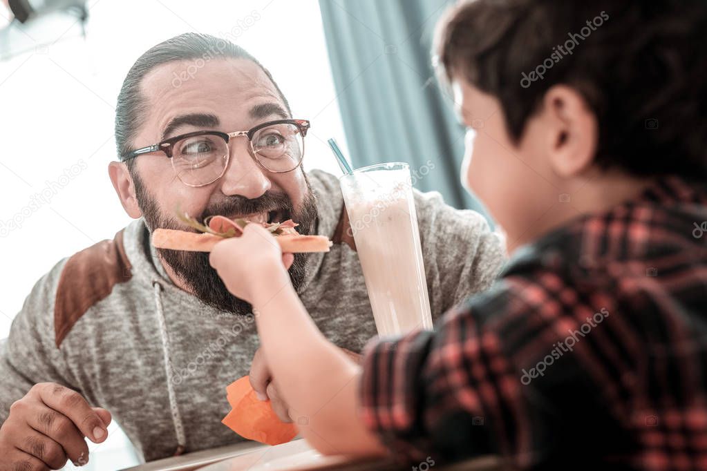 Cute generous son giving piece of pizza to his father