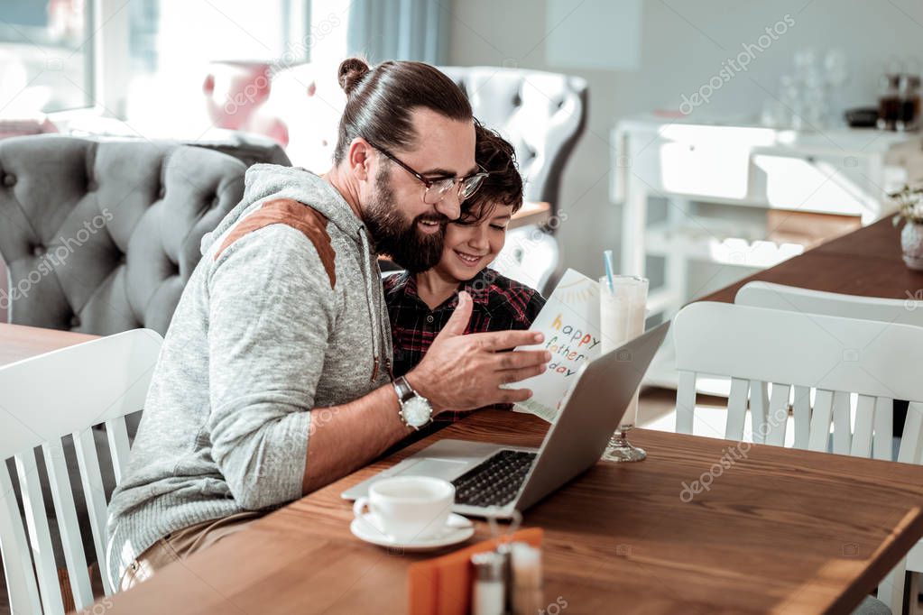 Bearded dark-haired father feeling surprised seeing postcard from son