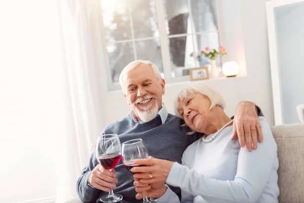 Sonriente pareja de cabello gris bebiendo vino tinto en casa — Foto de Stock