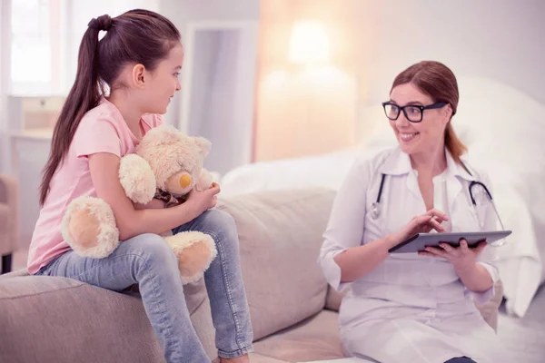 Profesionální rodinný lékař hostující roztomilá dívka sedí na pohovce s hračkou — Stock fotografie