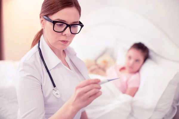 Médico profesional con chaqueta blanca mirando el termómetro sentado cerca de la chica — Foto de Stock