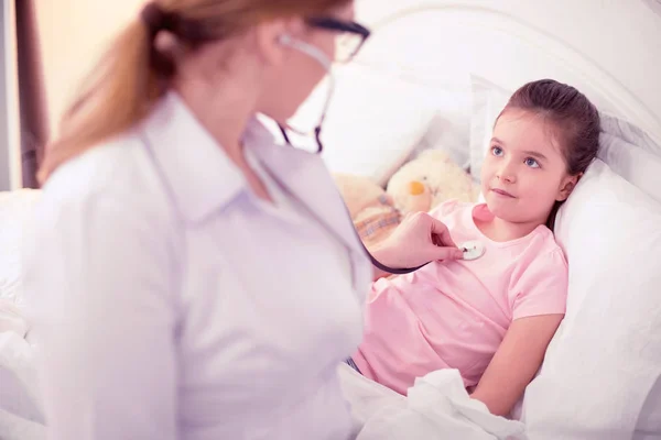 Erfahrener Arzt untersucht kleines krankes Mädchen, das im Bett liegt — Stockfoto