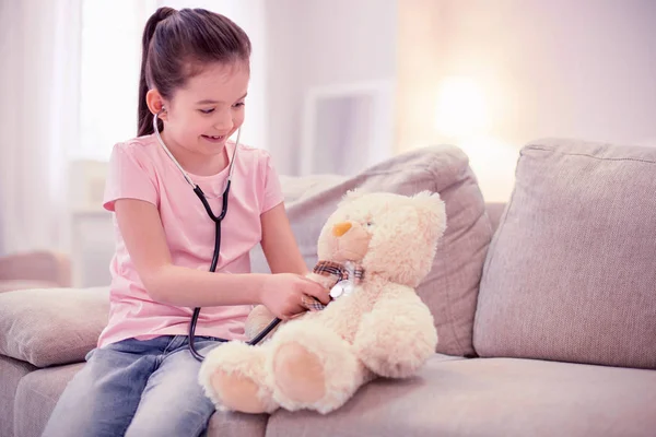 Dark-haired cute girl wearing jeans and pink shirt playing with teddy bear — Stock Photo, Image