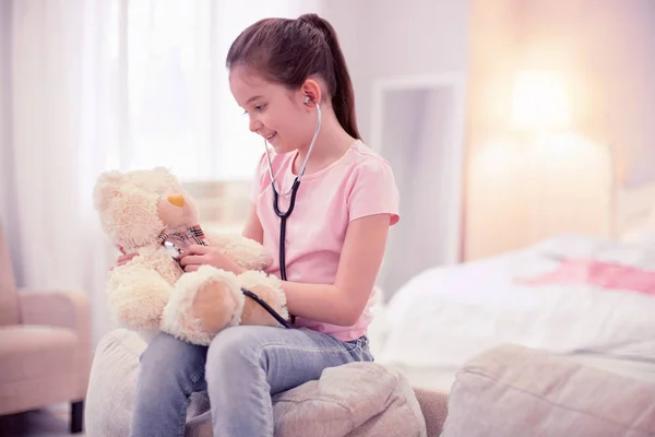 Gadis kecil berambut gelap duduk di sofa dan bermain dengan beruang — Stok Foto