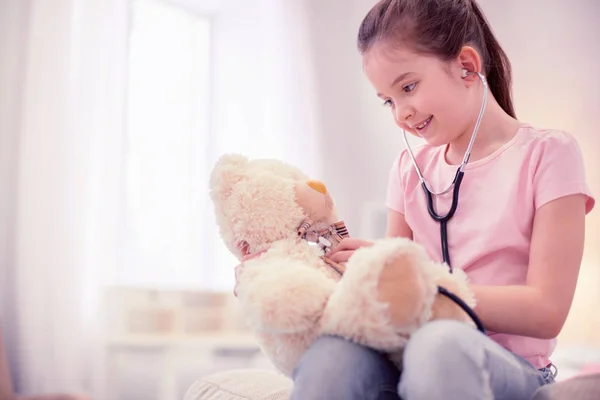 Cute preschool girl feeling entertained while playing with teddy bear — Stock Photo, Image