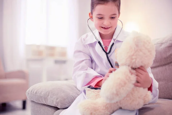 Cute beaming daughter of doctor playing examining teddy bear — Stock Photo, Image