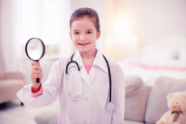 Маленькая девочка держит увеличительное стекло, притворяясь доктором — стоковое фото