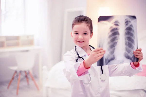 Donker-eyed preschool meisje dragen witte jas holding röntgenfoto van de longen Rechtenvrije Stockafbeeldingen