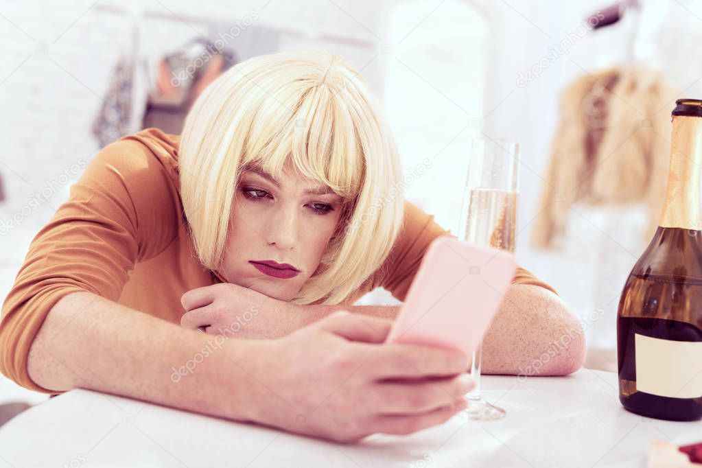 Attractive crossdresser with make up on texting with his smartphone
