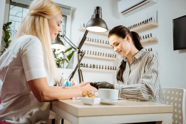 Pleasant dark-haired nail artist talking to her constant client while working