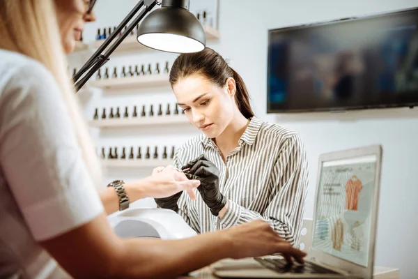 Dark-haired nail artist wearing stylish striped blouse working