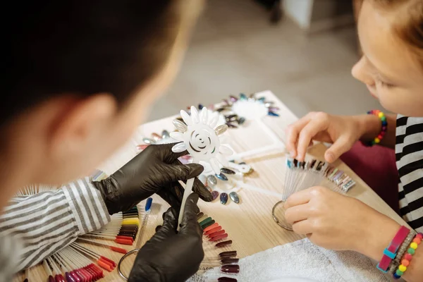 Dark-haired nail artist showing shades of beige her teenage client