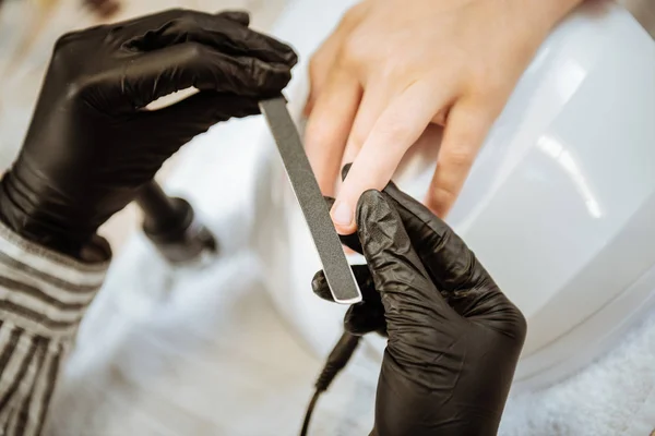 Close up of professional nail artist wearing black gloves holding nail file — Stock Photo, Image