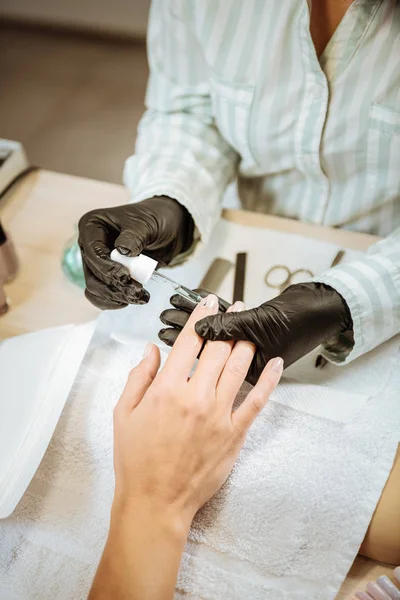 Профессиональная художница ногтей в черных перчатках раскрашивает ногти своей клиентки — стоковое фото