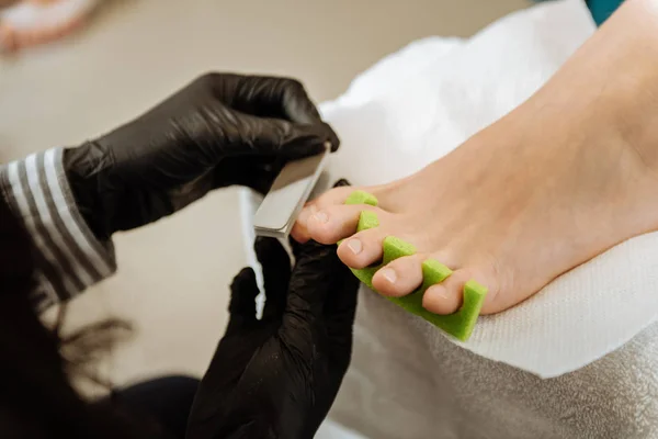 Chiropodist fazendo luvas pretas fazendo pedicure para seu cliente — Fotografia de Stock