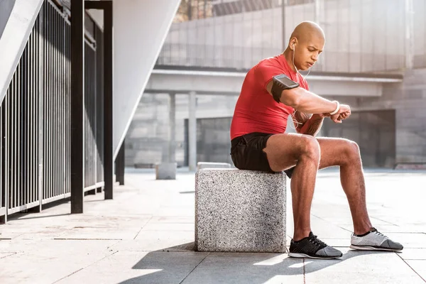 Příjemný mladý muž dívá na svůj fitness náramek — Stock fotografie