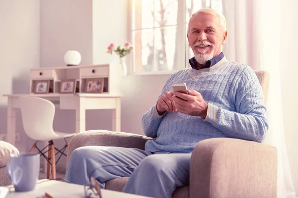 Smiling old man spending time with smartphone
