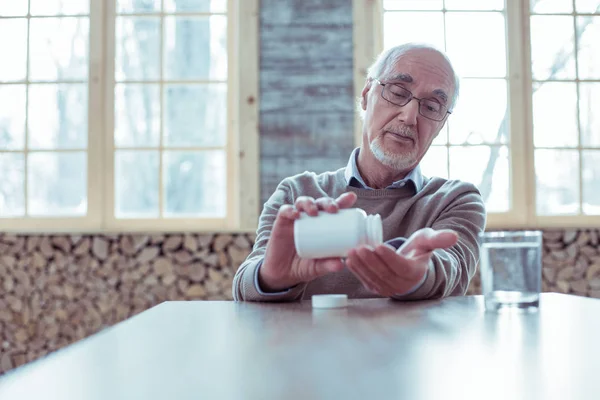Серйозний чоловік на пенсії дивиться в пляшку з медициною — стокове фото