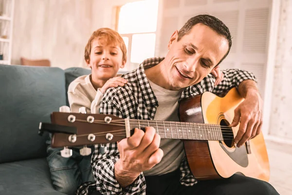 Glimlachend gefascineerd jongen observeren zijn vaders meesterlijke gitaar spelen. — Stockfoto