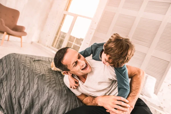 Energisk kid play-brottning med sin pappa på sängen. — Stockfoto