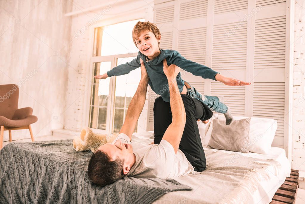 Excited little dreamer pretending to be an aeroplane while playing with his father.