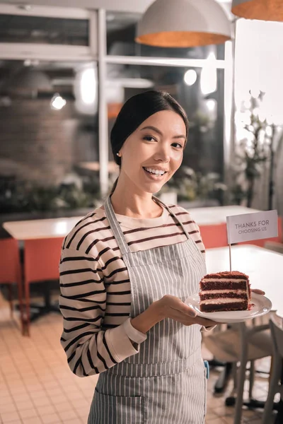 Appealing female entrepreneur holding tasty cake from her cafe