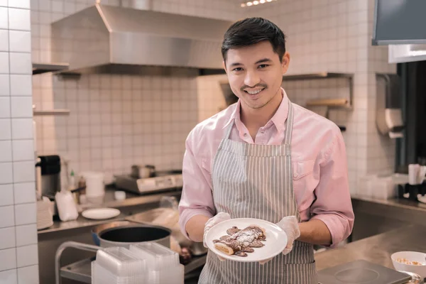 Smiling waiter holding white plate with pancakes for clients — Stock Photo, Image