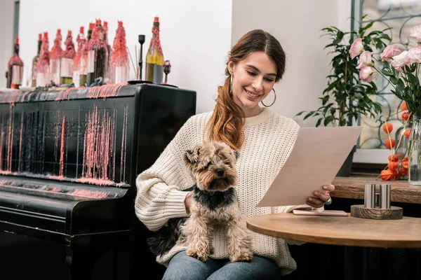 Woman reading the menu in the cafe holding her dog