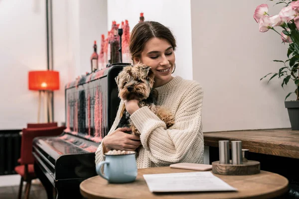 Жінка обіймає собаку, сидячи в кафе — стокове фото