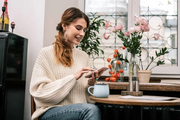 Mujer navegando por Internet usando un teléfono inteligente mientras bebe cacao — Foto de Stock