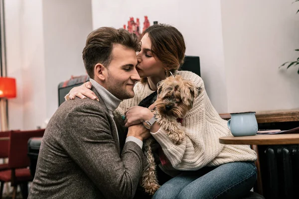 Женщина целует своего партнера, держа собаку — стоковое фото