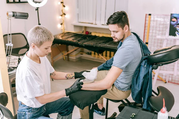 Professionele vrouwelijke tattoo meester sproeien van alcohol op de blote hand — Stockfoto