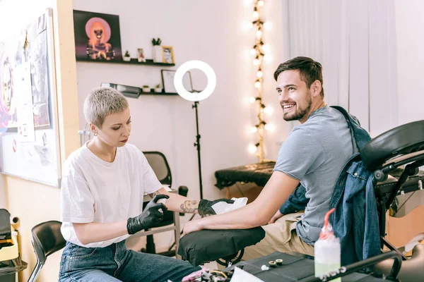 Sorrindo cliente de cabelos escuros sentado em cadeira especial e ficando pulverizado à mão — Fotografia de Stock