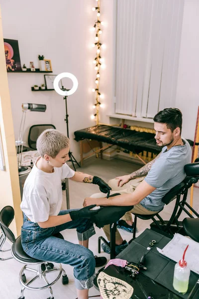 Atractivo maestro del tatuaje femenino que trabaja con el cliente de pelo oscuro — Foto de Stock