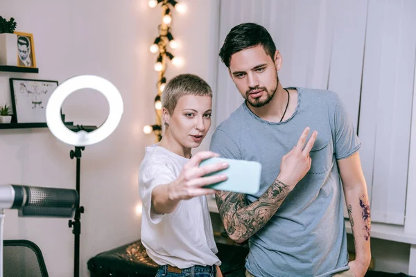 Loira tatuadora e seu cliente regular fazendo selfie após longa sessão — Fotografia de Stock