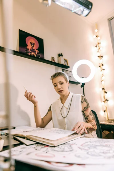 Short-haired female tattoo master sitting in her office corner and smoking — Stock Photo, Image