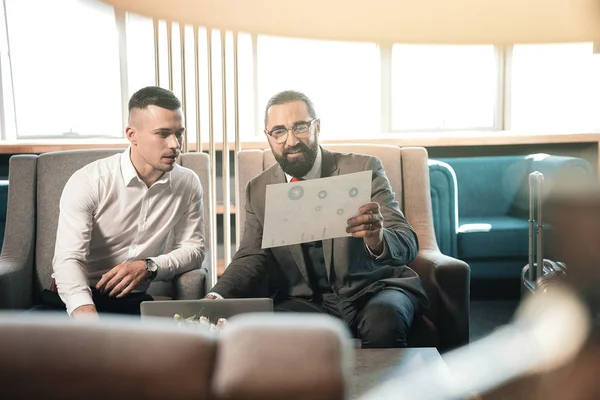 Investisseur barbu portant des lunettes assis près de son jeune stagiaire — Photo