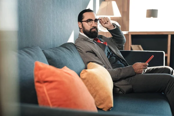 Hombre de negocios barbudo de cabello oscuro con traje sentado en el sofá — Foto de Stock