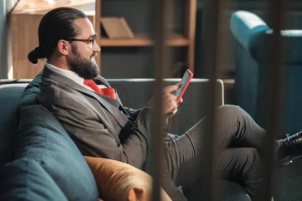 Skäggiga affärsman klädd i grå kostym och röd slips håller sin telefon — Stockfoto
